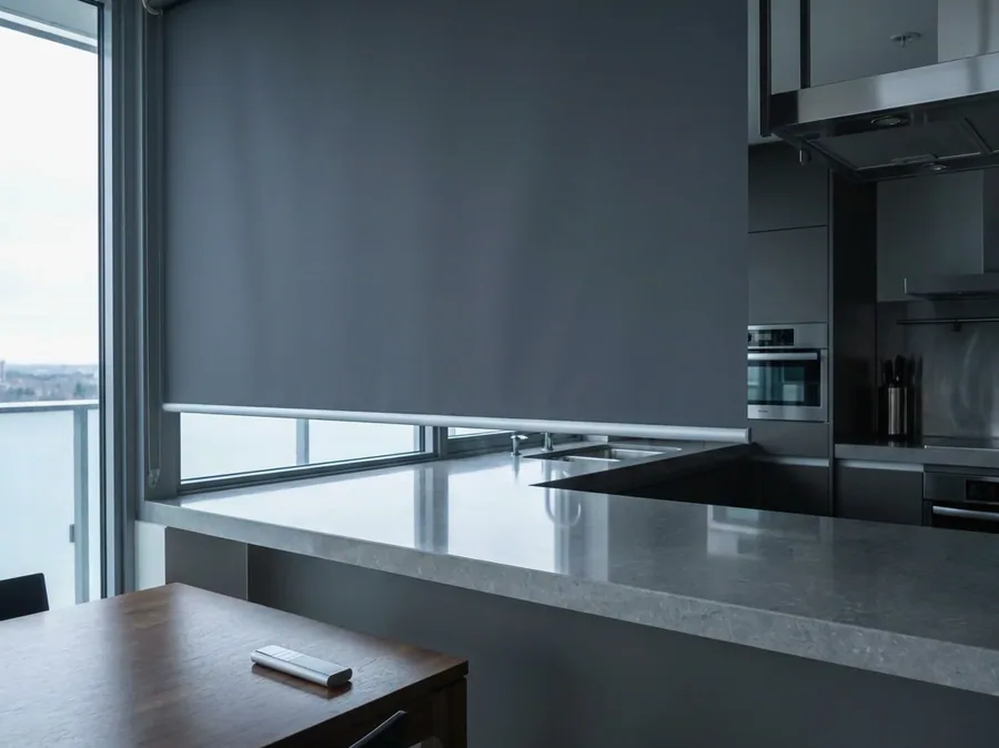 Motorised roller blind lowered across a kitchen window, its remote resting on the table — no cords or chains